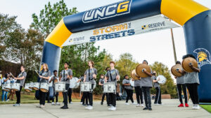 UNCG's drum section marches through a Spartan-themed arch on the sidewalk during Storm the Streets.