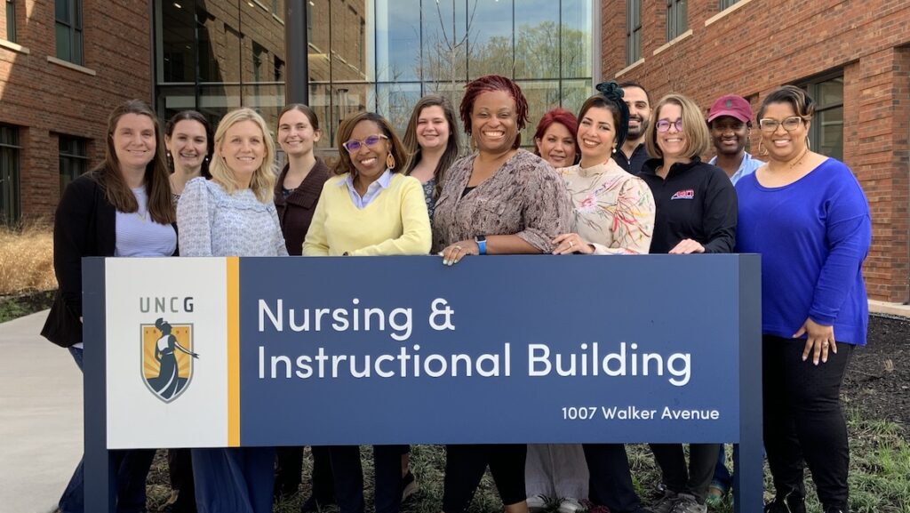 UNCG SON students and staff stand behind Nursing and Instructional building sign.
