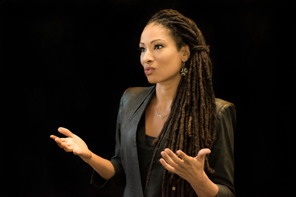 Ruha Benjamin picture (hands held up with palms facing sky)