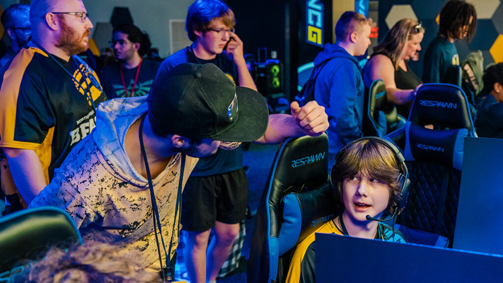 Adult coaches a student gamer in the esports arena.