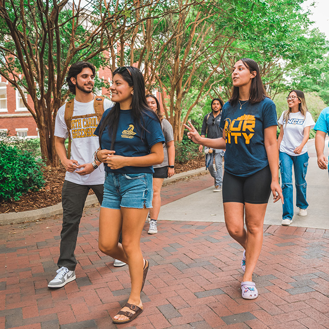 Students walk through campus in UNCG t-shirts.