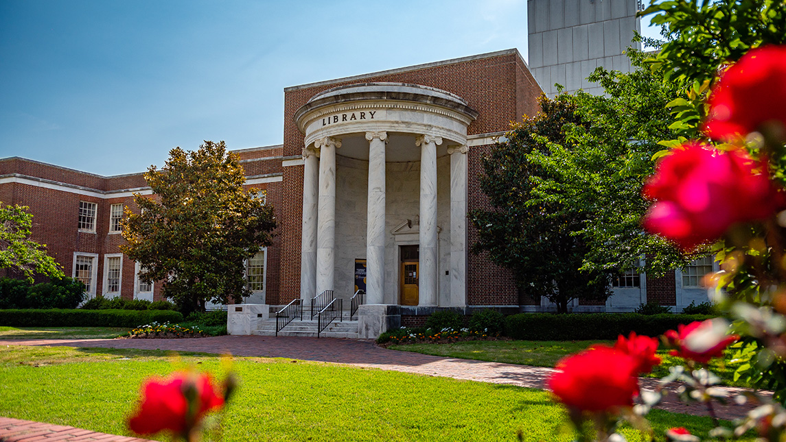 Red flowers bloom outside the UNCG library building.