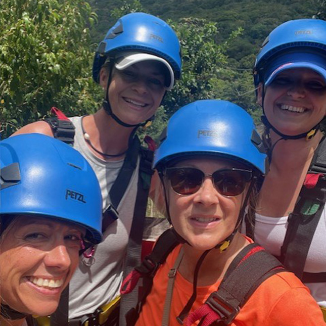 4 women with safety helmets and zipline harnesses on.