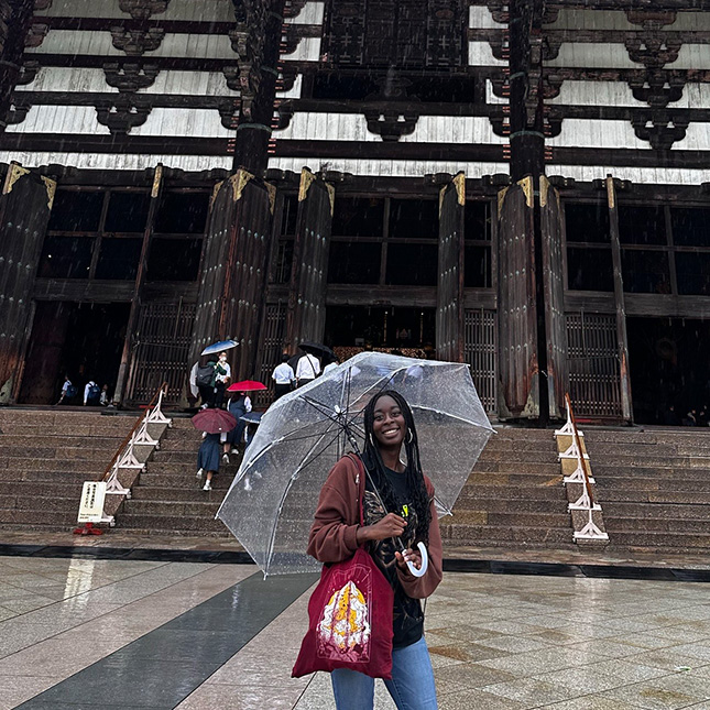 Young woman under an umbrella poses in front of a traditionally decorated building in Asia.