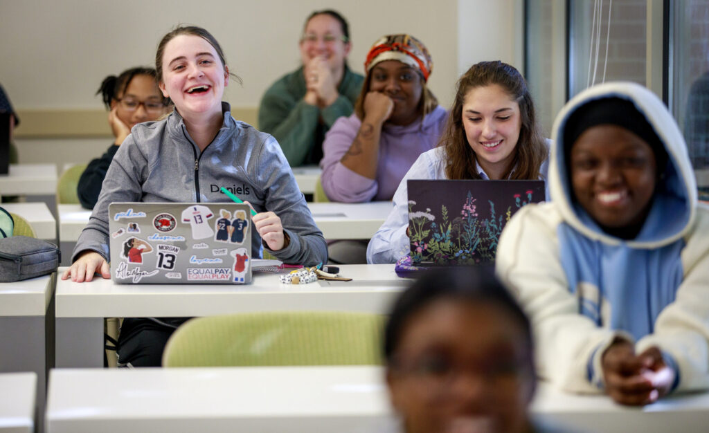 Smiling students sitting in rows of desks with laptops.