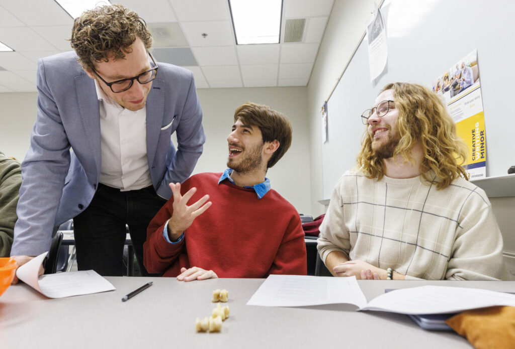 Assistant Professor Michiel Van Veldhuizen watches his students Ethan Devon and Jamie Gross who are playing with ancient dice.