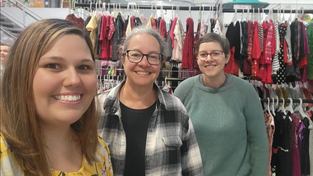 UNCG staff take a selfie beside the clothing racks at the Family Room in Greensboro.