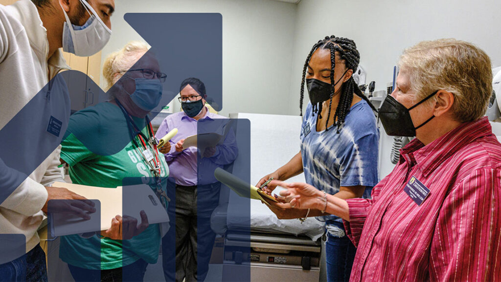 Five UNCG researchers in masks talk inside a medical exam room.