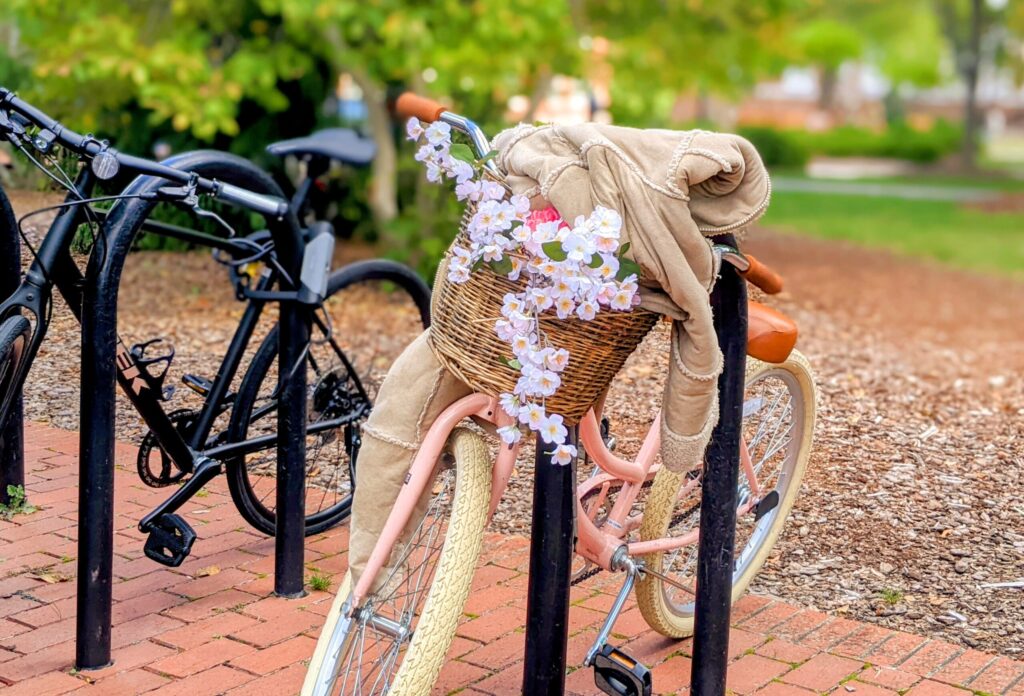 A pink bicycle with flowers adorning the basket and a jacket draped over its handlebars.
