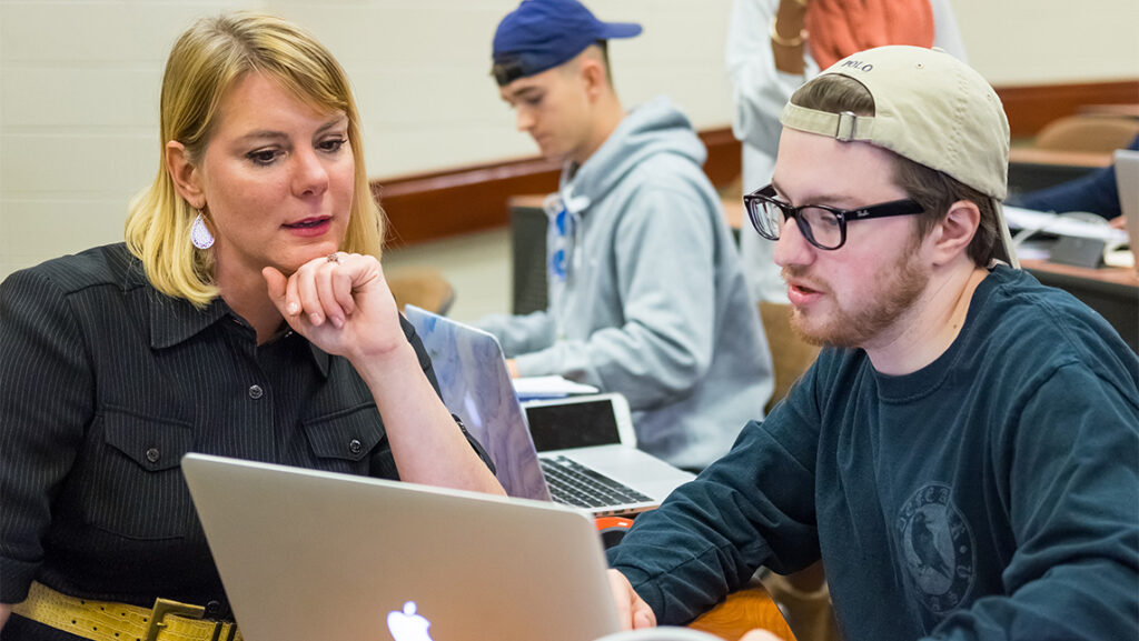 UNCG faculty member Sara MacSween works with a student in a conference-style classroom.
