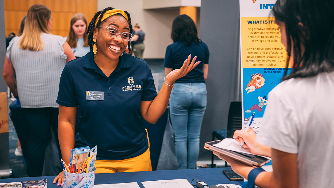 A person smiles with her hand up at the UNCG Be Well, Stay Well event