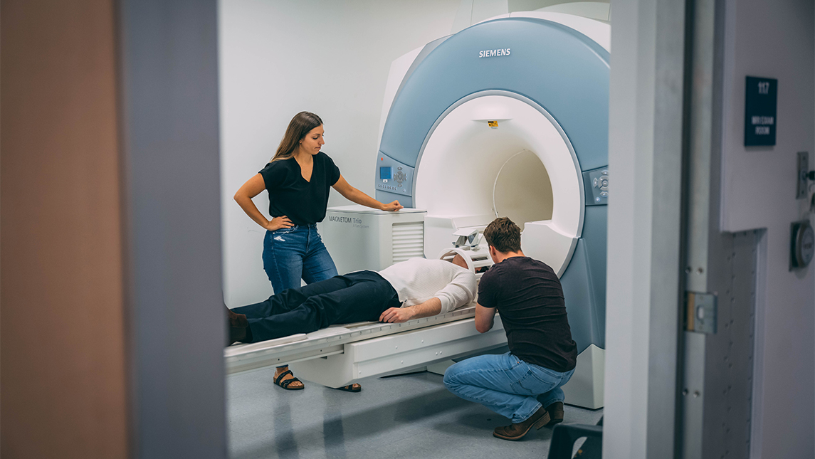 A person uses the MRI machine as two additional people assist.