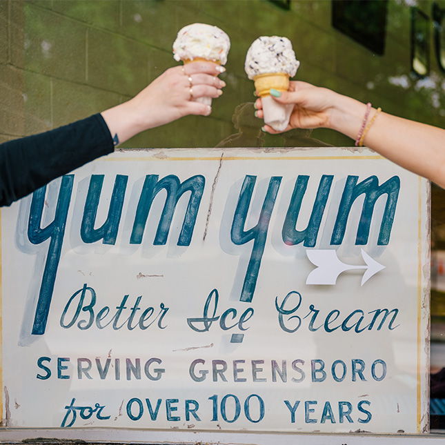 Arms come in from either side holding ice cream cones over a Yum Yums sign that says "serving Greensboro for over 100 years."