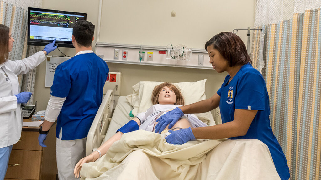 Three UNCG nursing students practice caring for a mannequin patient in a bed.