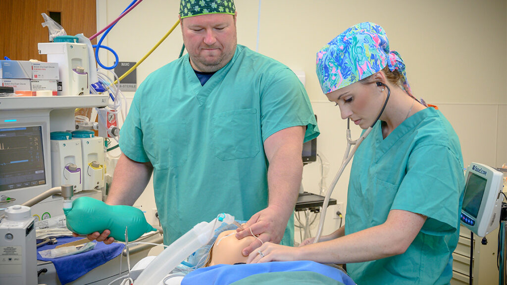 Two UNCG nurse practitioner anesthesiology students attach a mask to a mannequin.