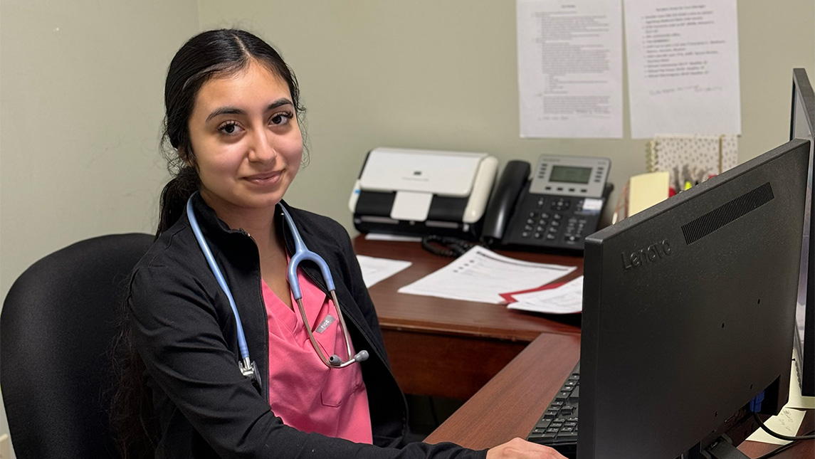 UNCG alumna Catlin Torres ’23 sits at a desk in a health clinic.