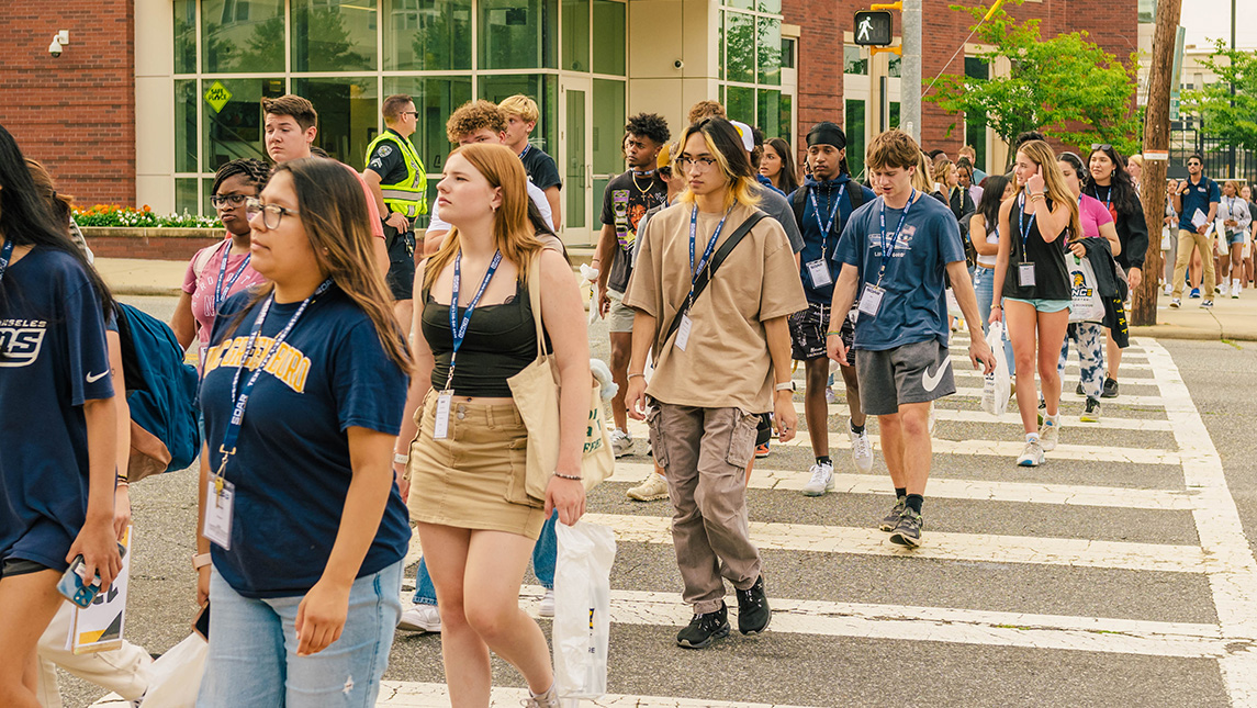 A line of new UNCG students cross a street.