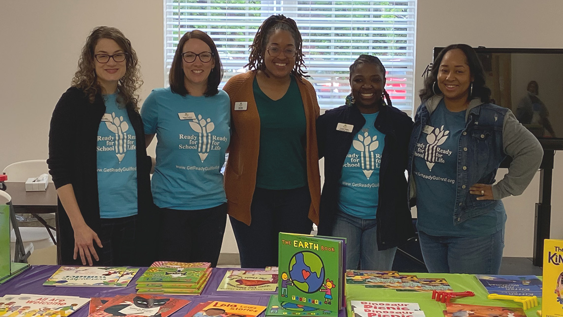 Dr. Tyla Ricks, UNCG alumna, takes a group photo at a table full of children's books with four colleagues with Ready for School, Ready for Life.