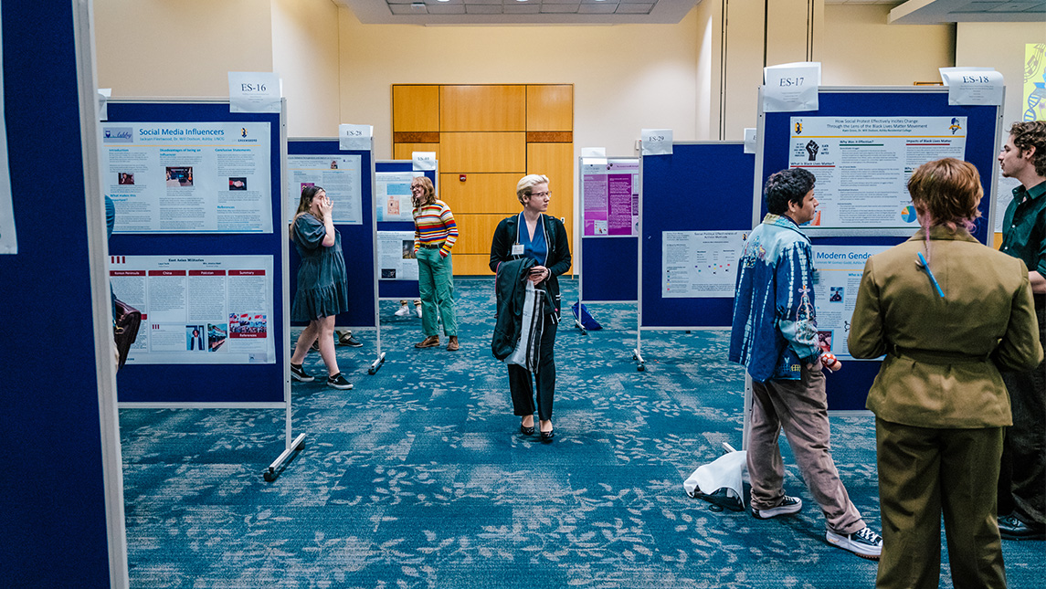A woman walks past a line of poster boards displays in UNCG's Cone Ballroom.
