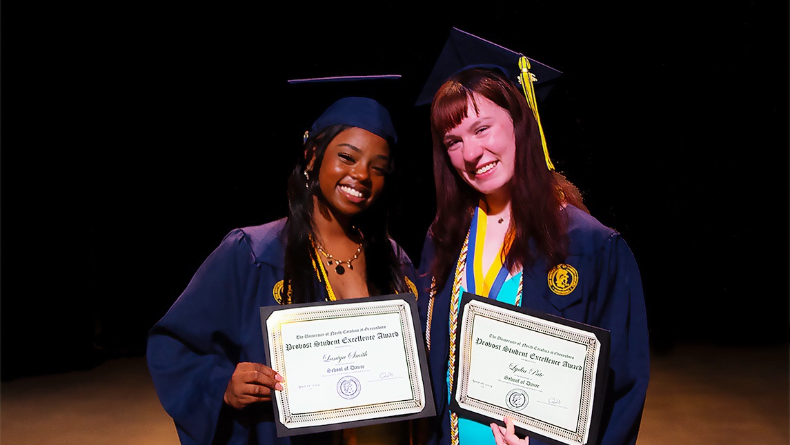 UNCG students Laniya Smith and Lydia Pate in their caps and gowns holding certificates.