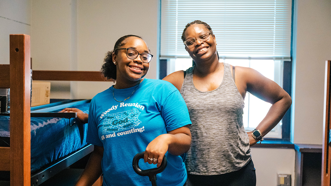 Student poses in her new room with her mother as she moves into her residence hall.