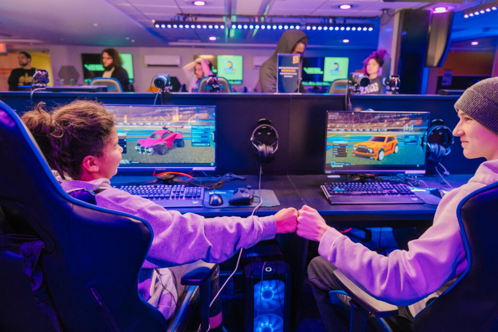 Students fist bump as they sit in front of monitors in the esports arena and play Rocket League.
