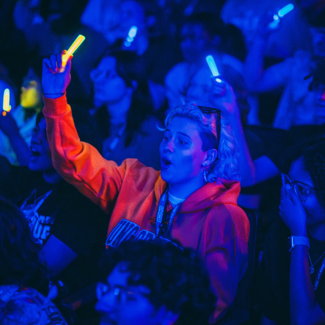 Student waves a glowstick in the dark EUC sitting in the crowd of other students with glowsticks. 