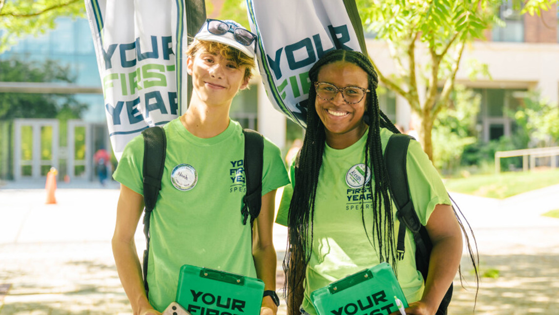 Two UNCG volunteers wear green Spear t-shirts on campus.