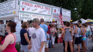 Crowds walk past a booth advertising fried apple pie.
