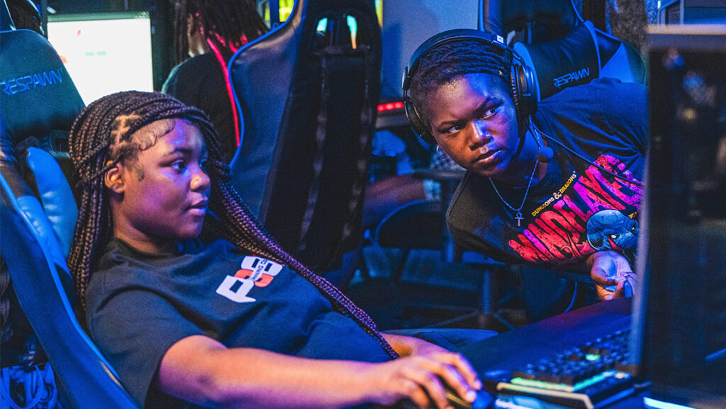 A girl looks at another girl's screen while they play games at the UNCG Esports Arena.