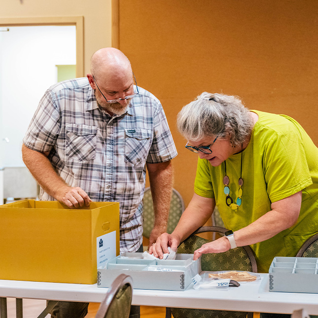 A man and a woman browse artifacts in boxes on a table at the Old Salem Visitor Center.