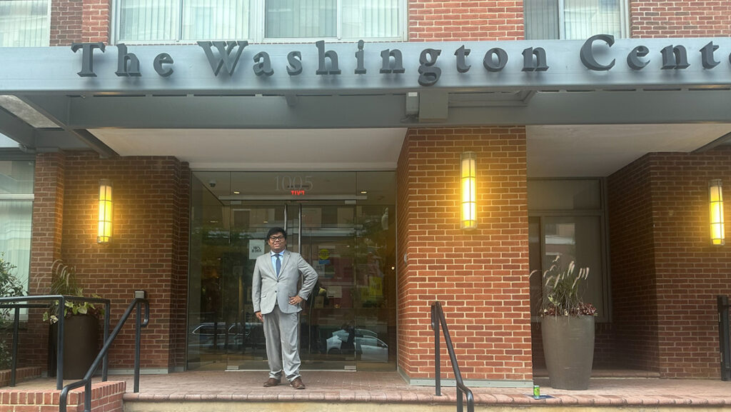 Young man in suit stands at the entrance of a building with "The Washington Center" sign overhead.