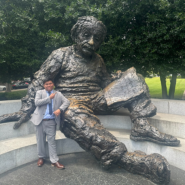 Young man in suit stands in front of a statue of Einstein in Washington, DC.