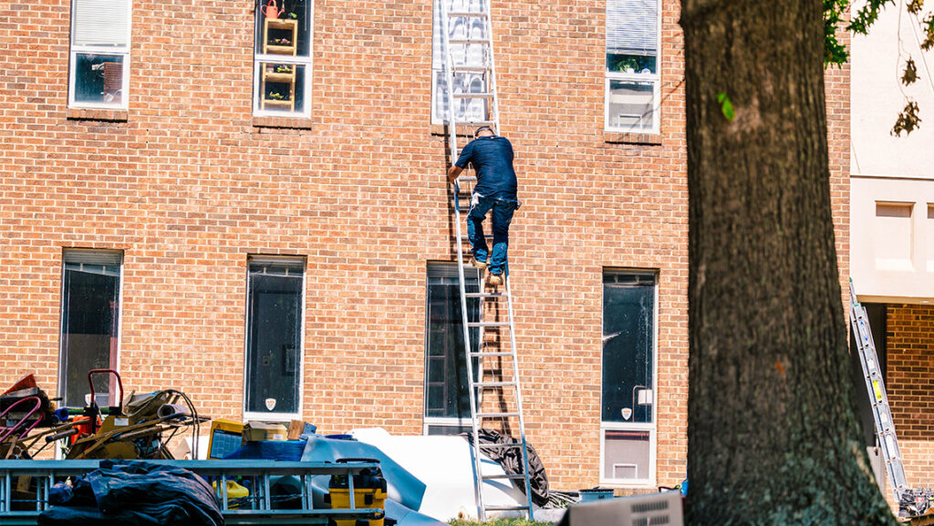 A construction worker climbs a ladder along UNCG's Mossman building.