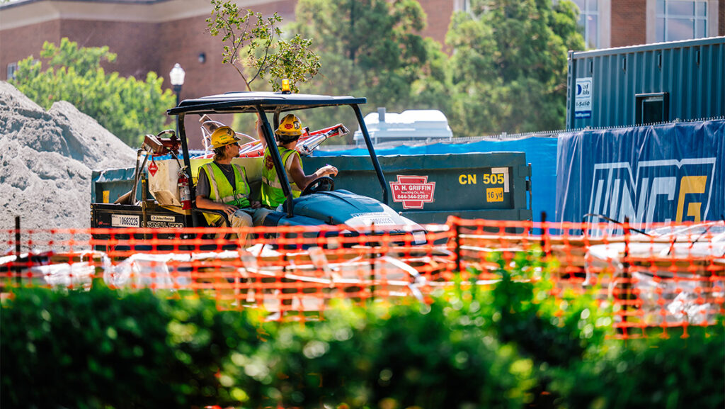 Construction crews drive a 6-wheeler through a construction zone at UNCG.