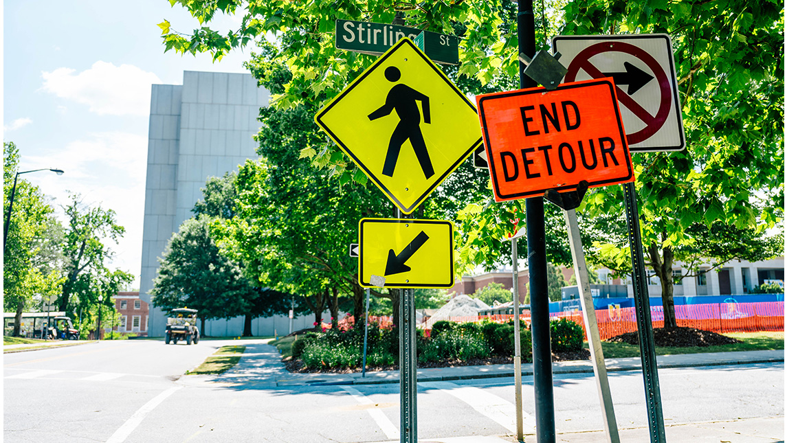 A walking man sign for a street at UNCG stands next to an "End detour" sign.