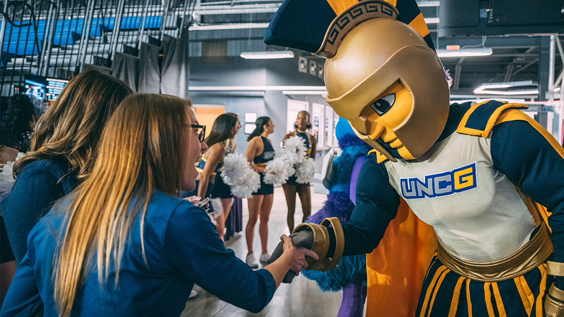 Spiro the UNCG mascot fistbumps a woman at the Swarm baseball stadium.