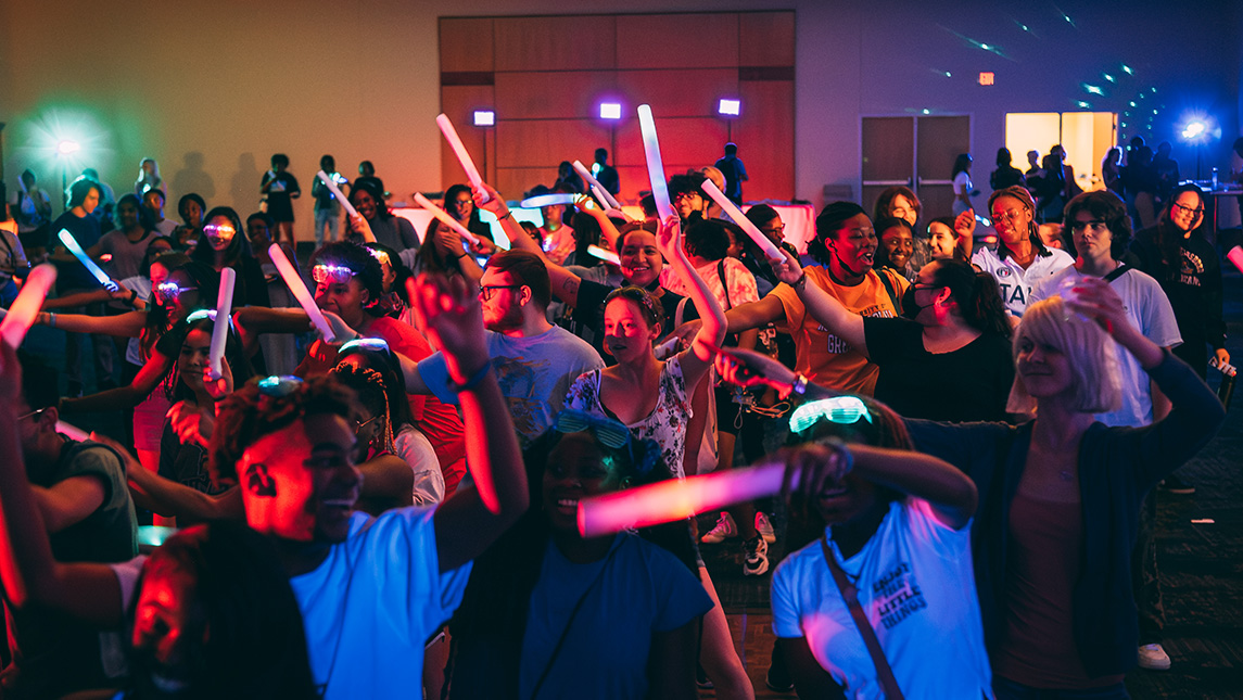 UNCG students with glowsticks dance at a block party.