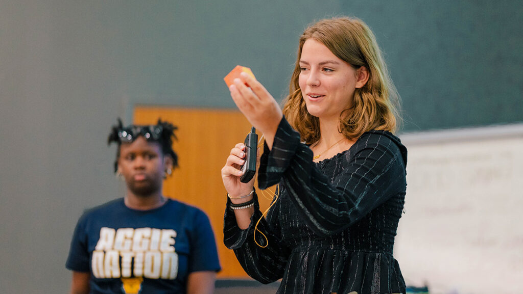 A high school student holds up a prototype sensor during a presentation.