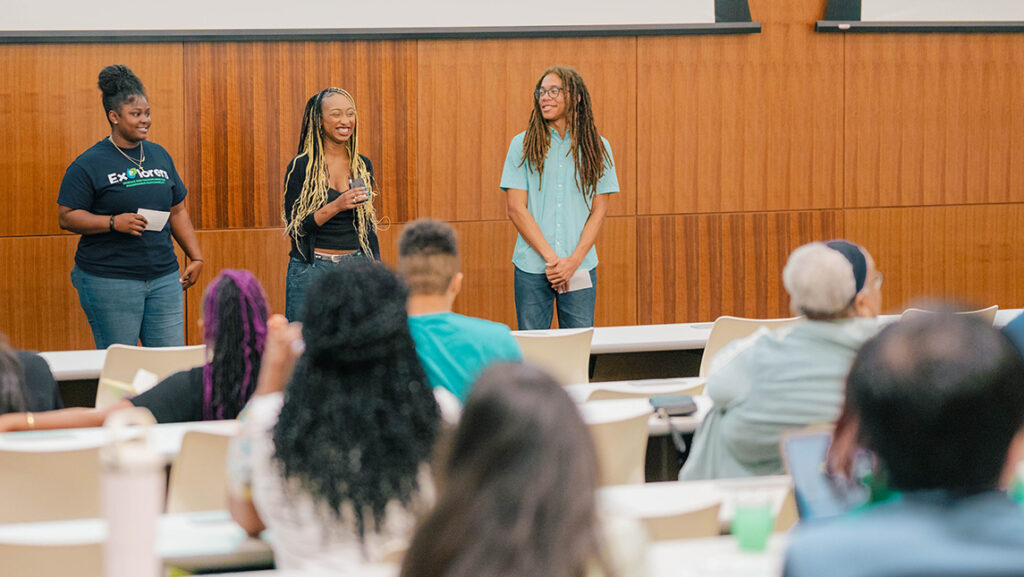 Three high school students present to an audience in a classroom.