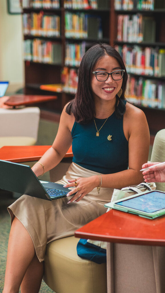 A student has her laptop open while smiling at a person who is outside of the frame.