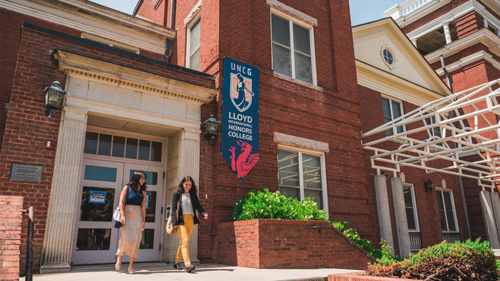 Two students walk outside of a red brick building.