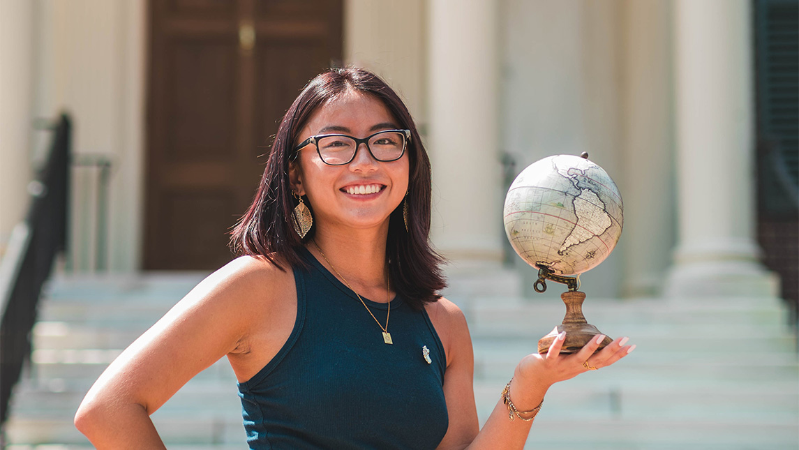 A headshot of a student holding a small globe in one hand.