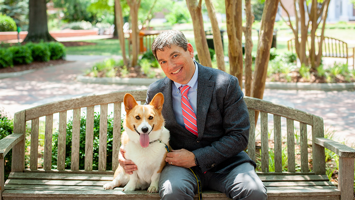 A man sits with a dog on a bench.