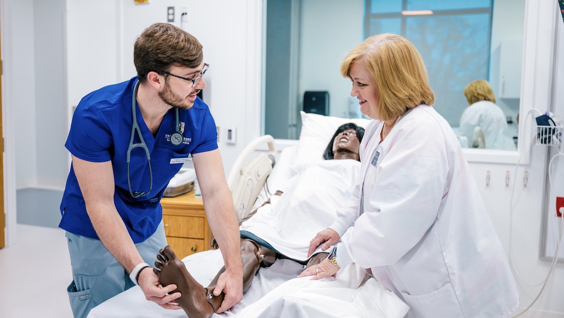 Female nursing professor assists a male nursing student with a nursing Mannequin