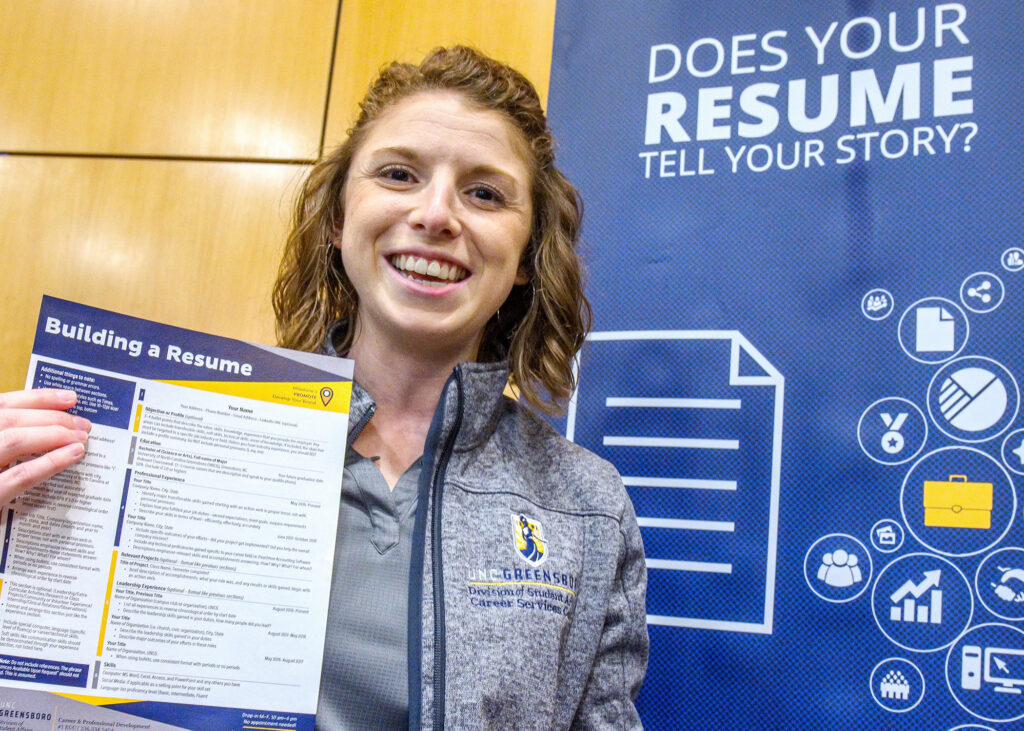 Woman in a UNCG shirt holds up a paper about resume building.