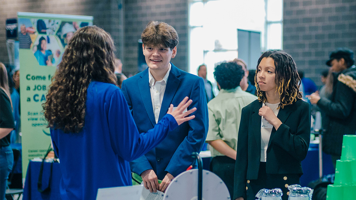 Students dressed in business suits talk to an employer at a career fair at UNCG.