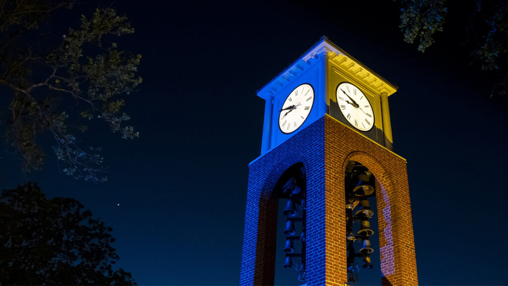 Blue and gold lights shine upon the UNCG Vacc clock tower.