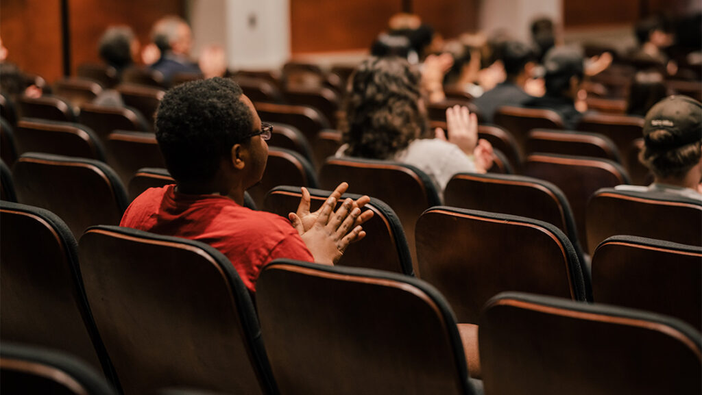 Students clap in their theatre seats during a talk at UNCG.