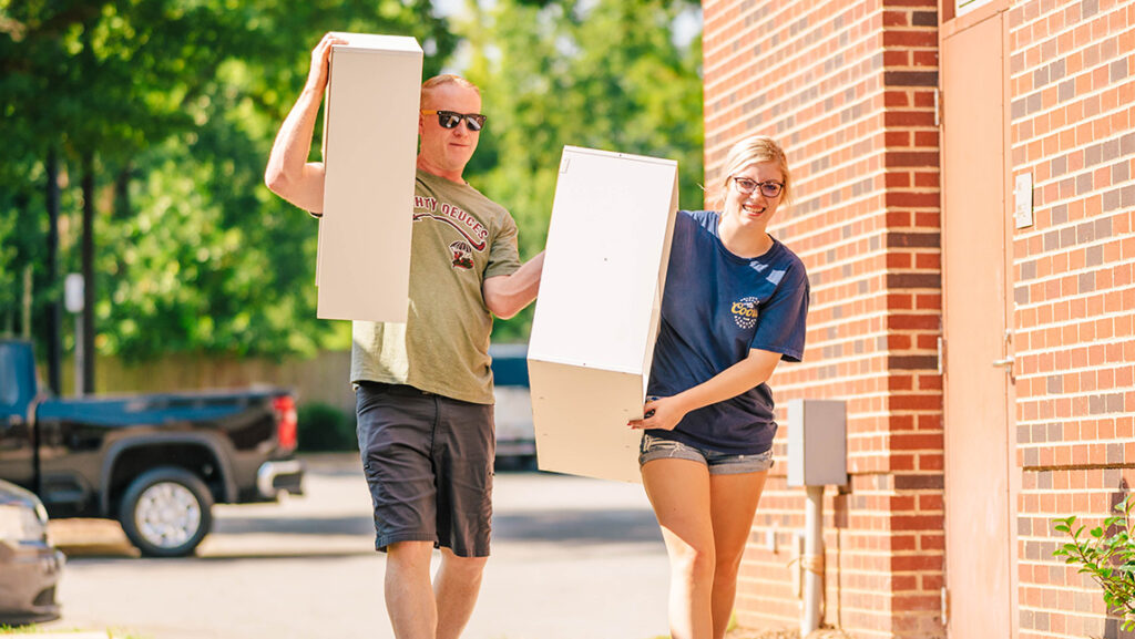 A new UNCG student and her father carry bookshelves outside.